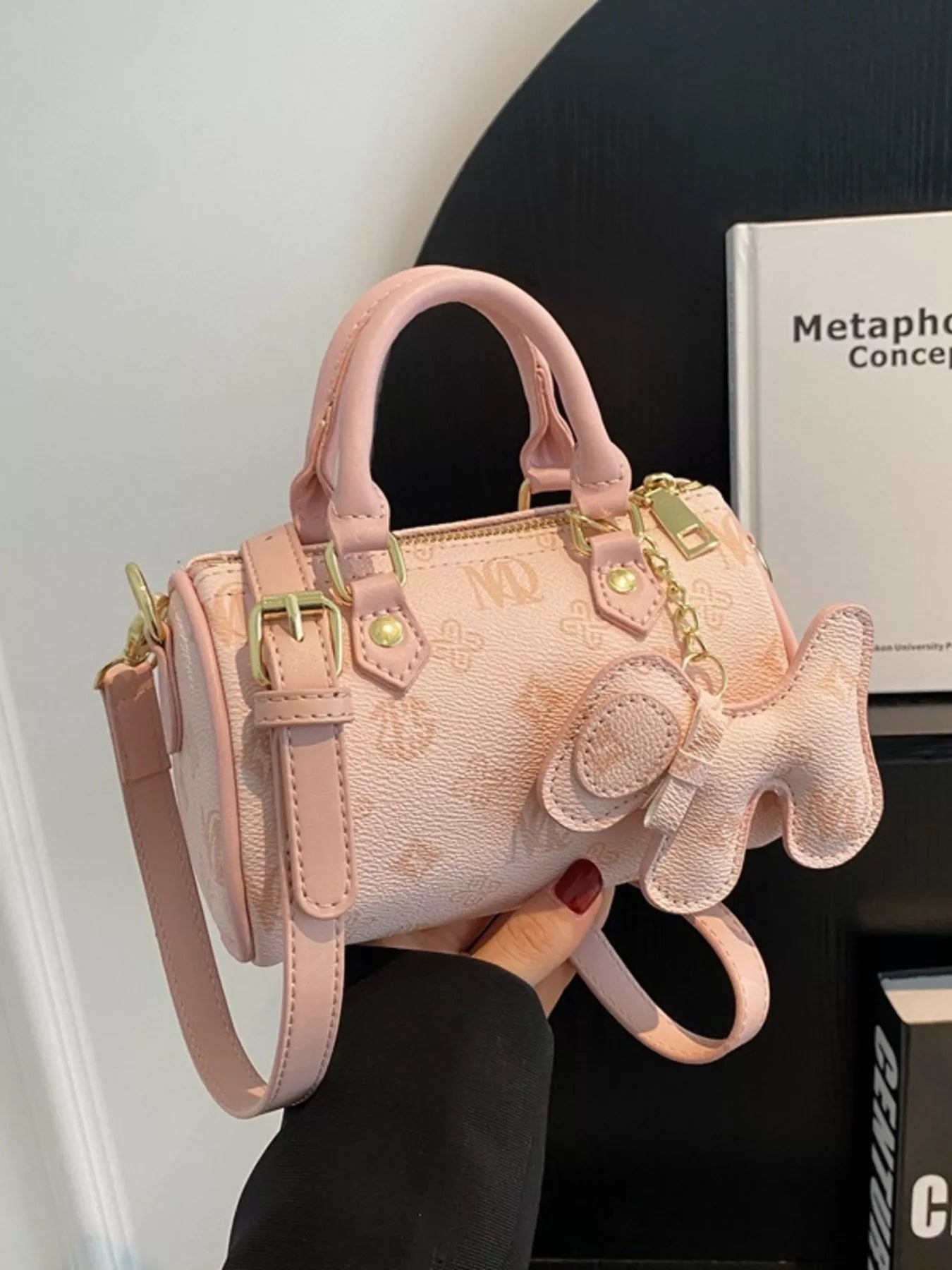 Pink handbag with decorative bow held by a person against a neutral background