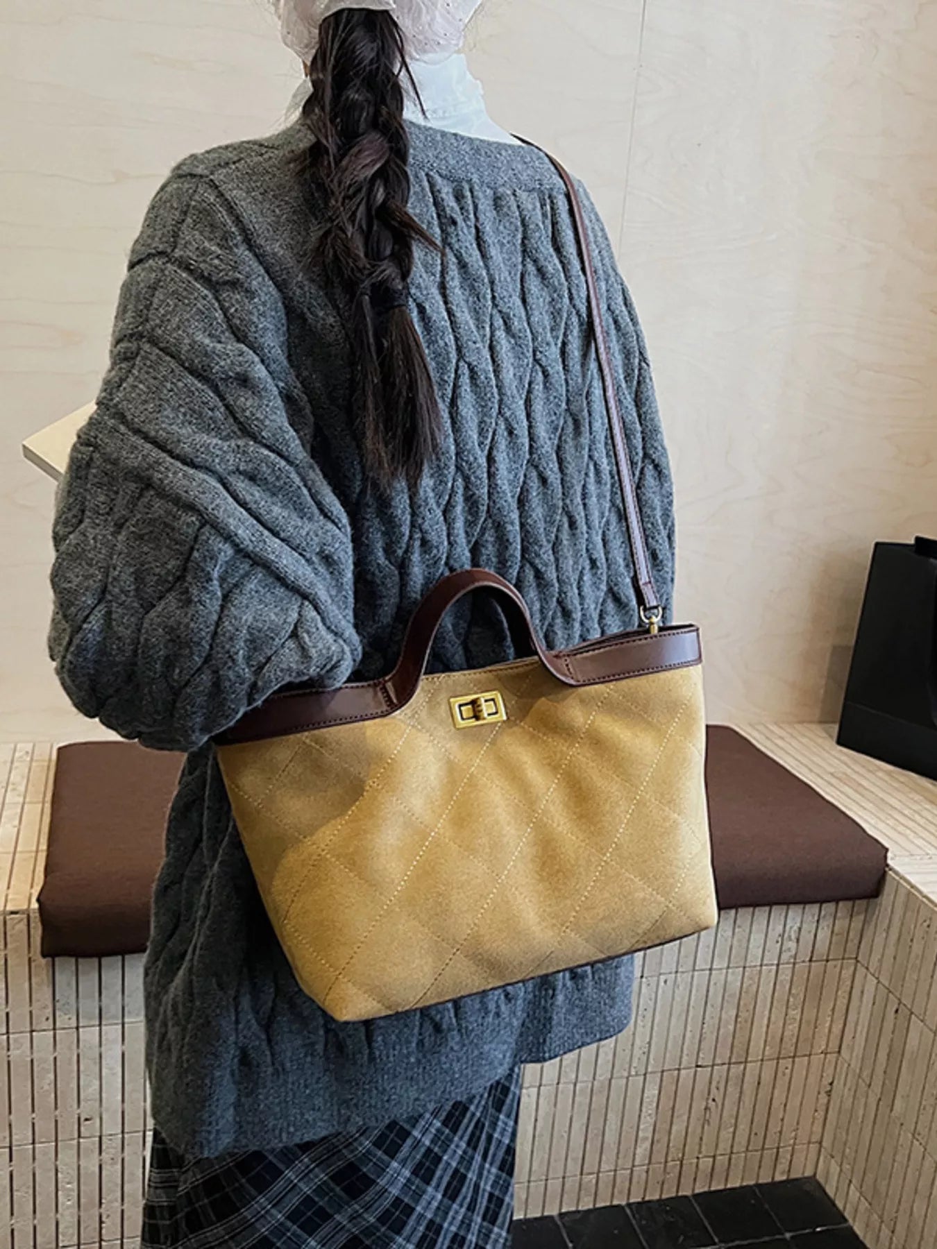 Person holding a tan leather handbag with a brown handle in a bathroom setting.