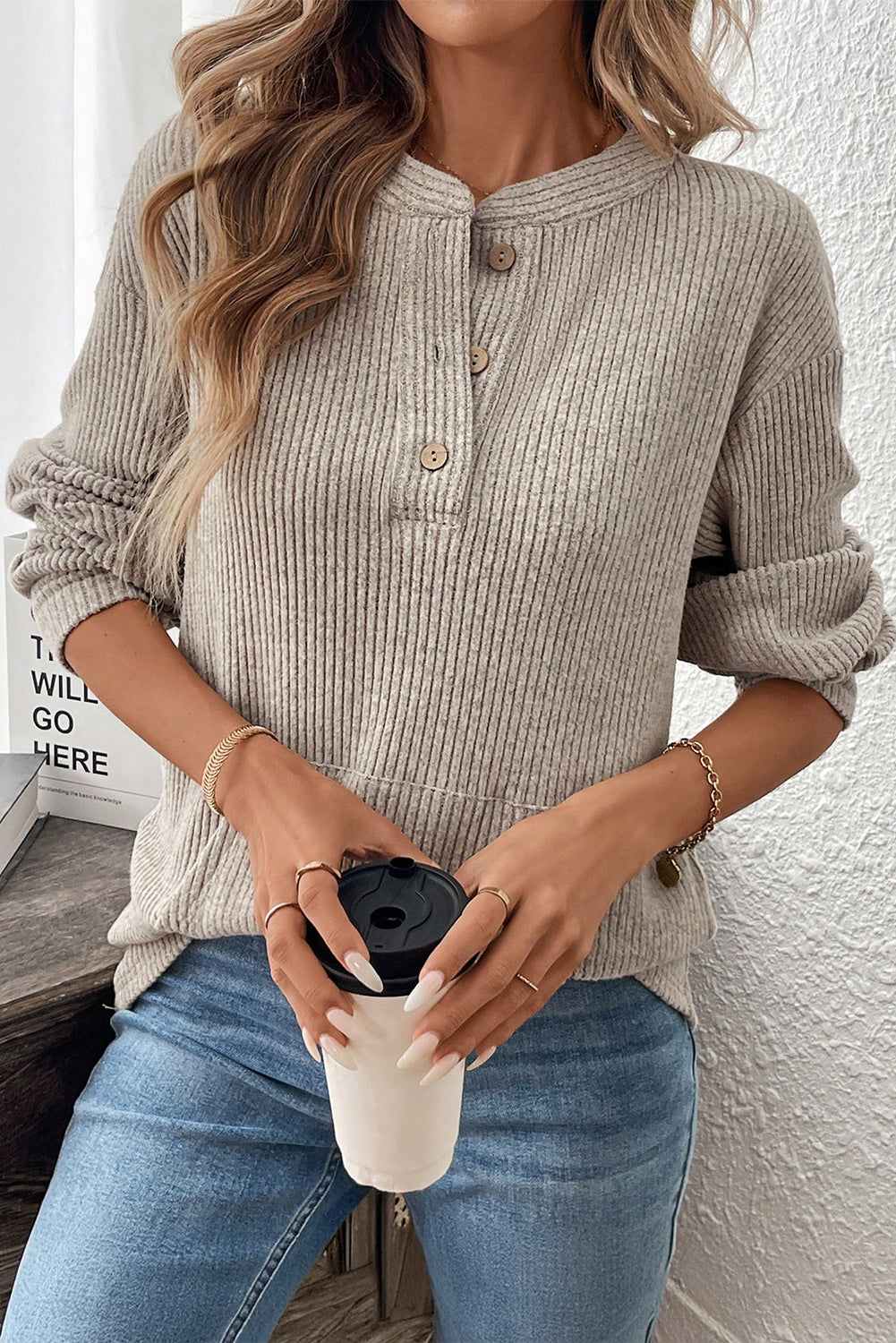 Person wearing a beige ribbed sweater and blue jeans, holding a coffee cup.