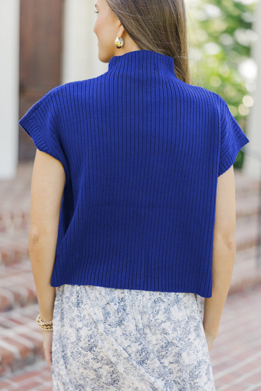 Woman wearing a blue ribbed sweater and floral skirt outdoors.