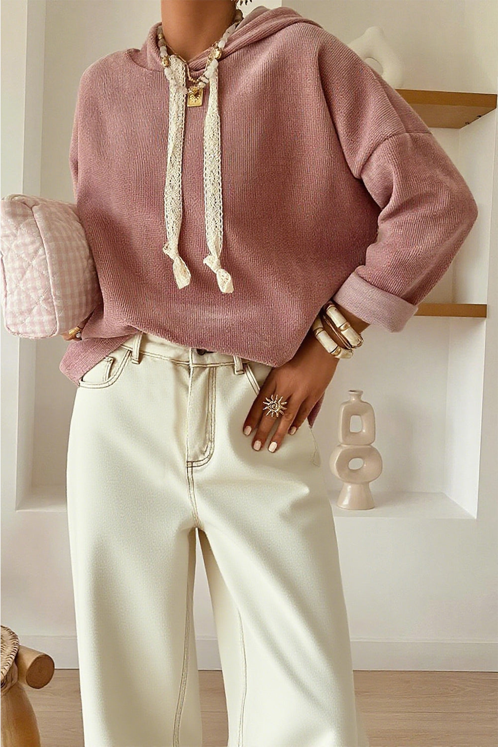 Person wearing a pink hoodie and light-colored pants in a minimalistic room.