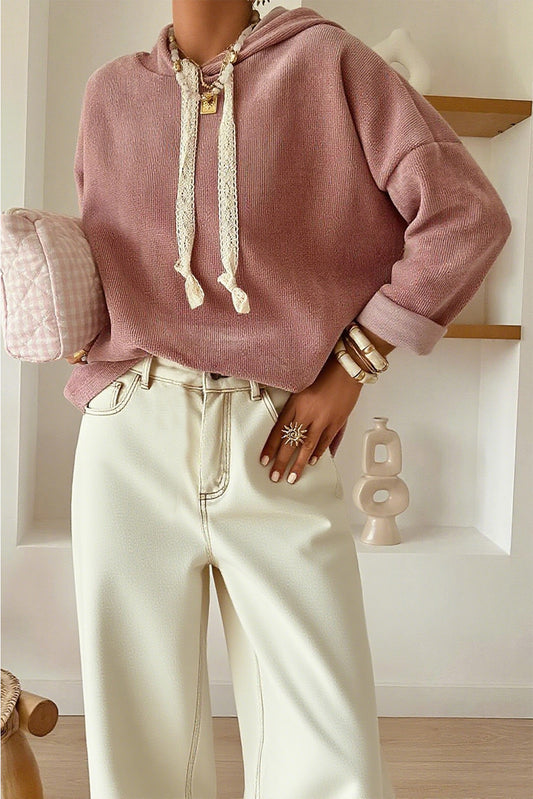 Person wearing a pink hoodie and light-colored pants in a minimalistic room.