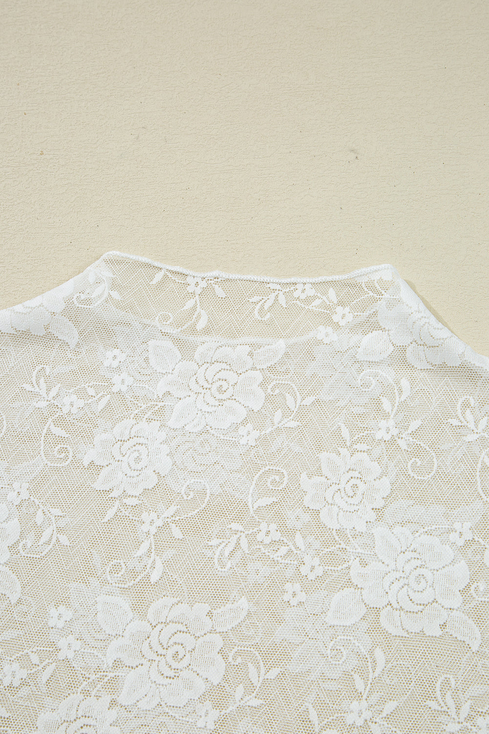 Close-up of a white lace fabric with floral patterns on a beige background