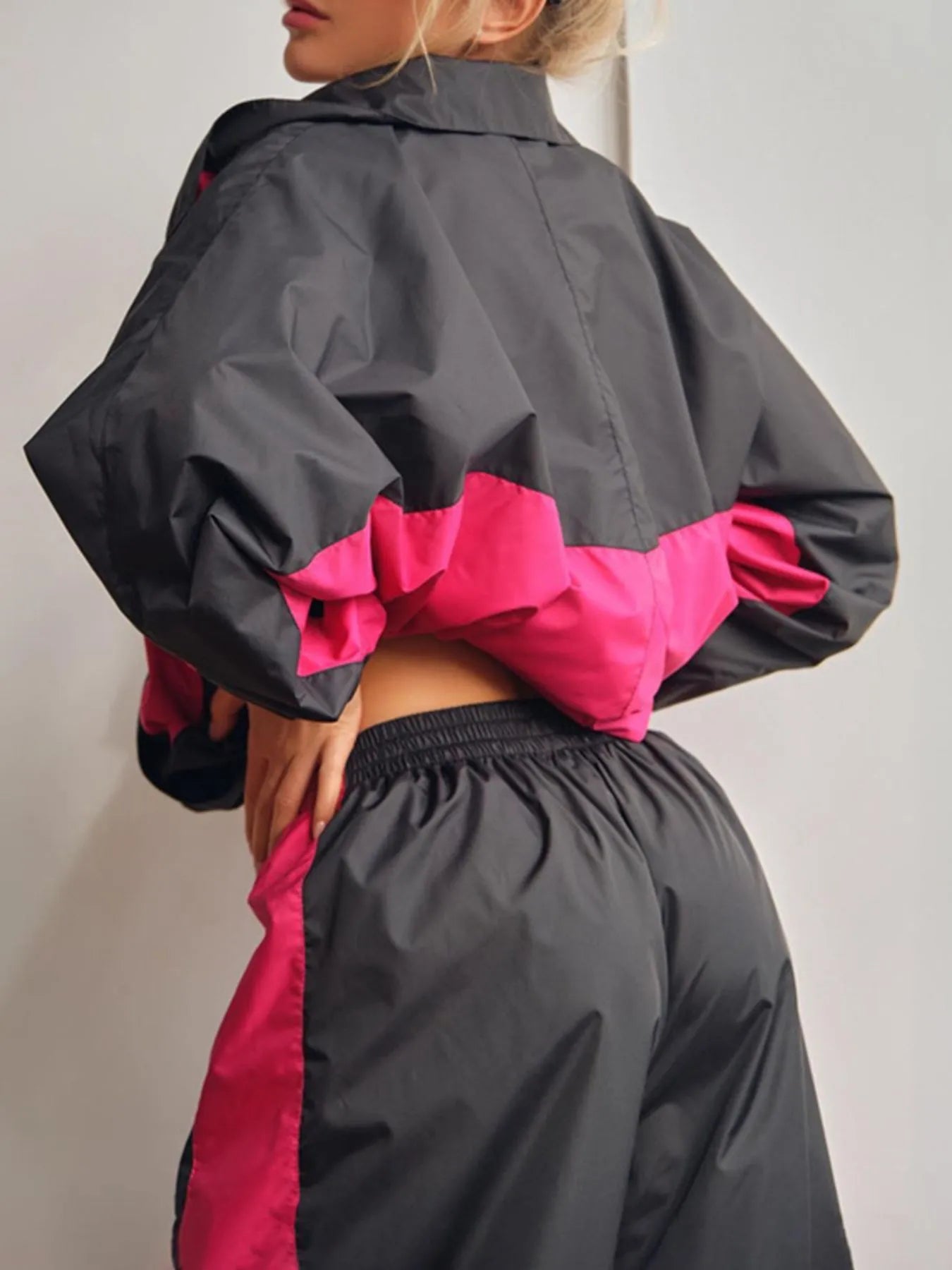 Person wearing a black and pink two-tone jacket and pants against a plain background
