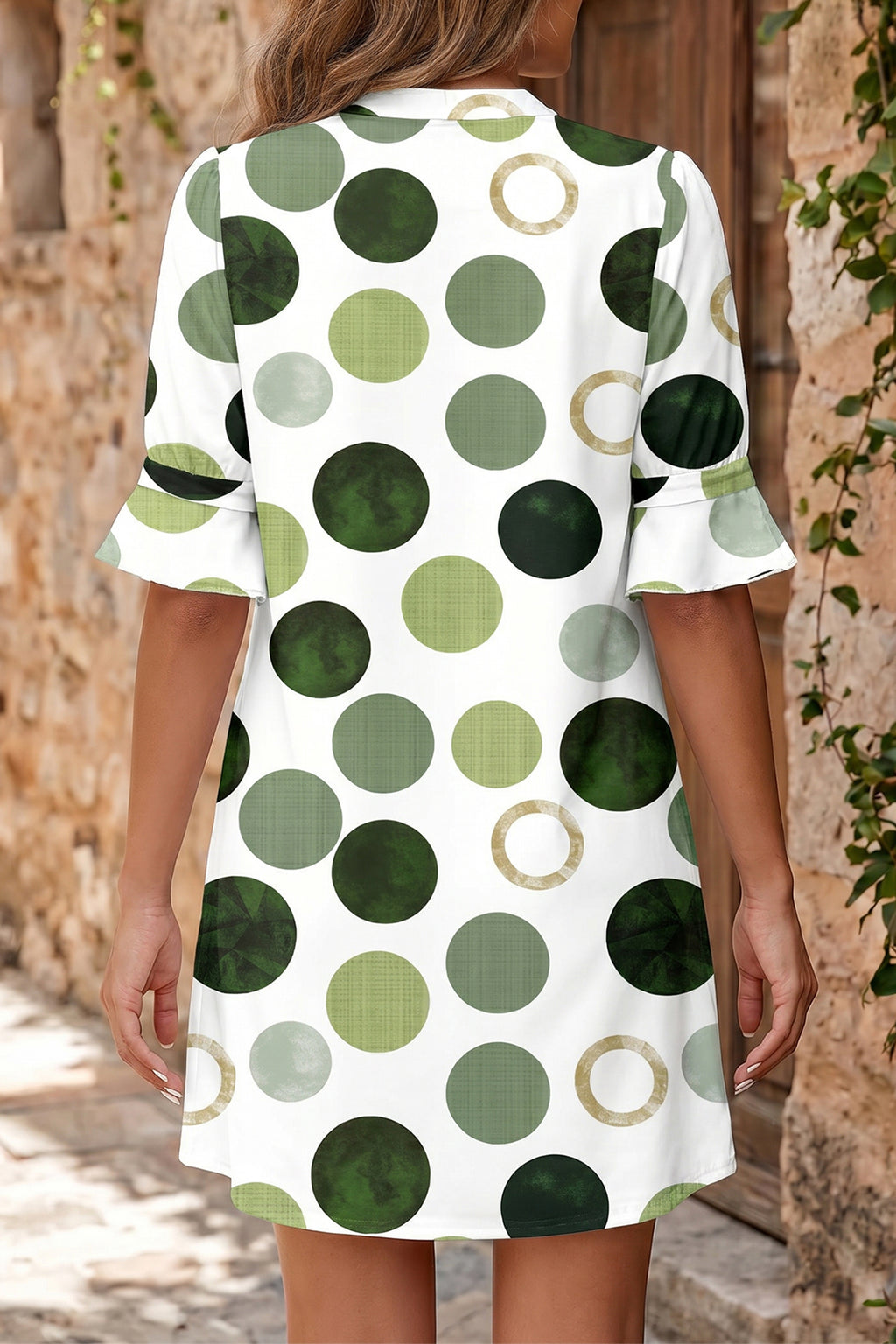 Person wearing a white dress with green and brown polka dot pattern outdoors. Back view