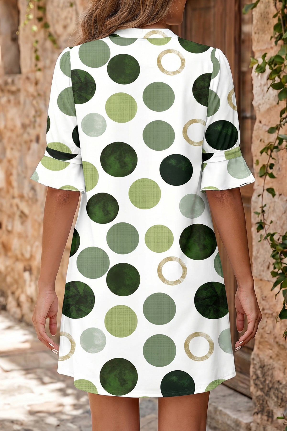 Person wearing a white dress with green and brown polka dot pattern outdoors. Back view