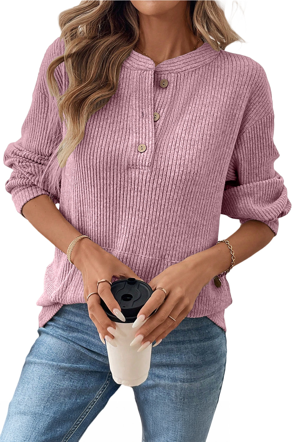 Person wearing a pink ribbed sweater holding a beige mug with a black lid.
