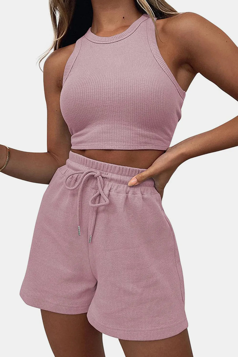 Person wearing a pink ribbed tank top and shorts set on a plain background