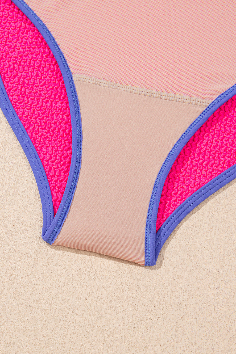 Close-up of a swimsuit top with pink and blue trim on a beige background
