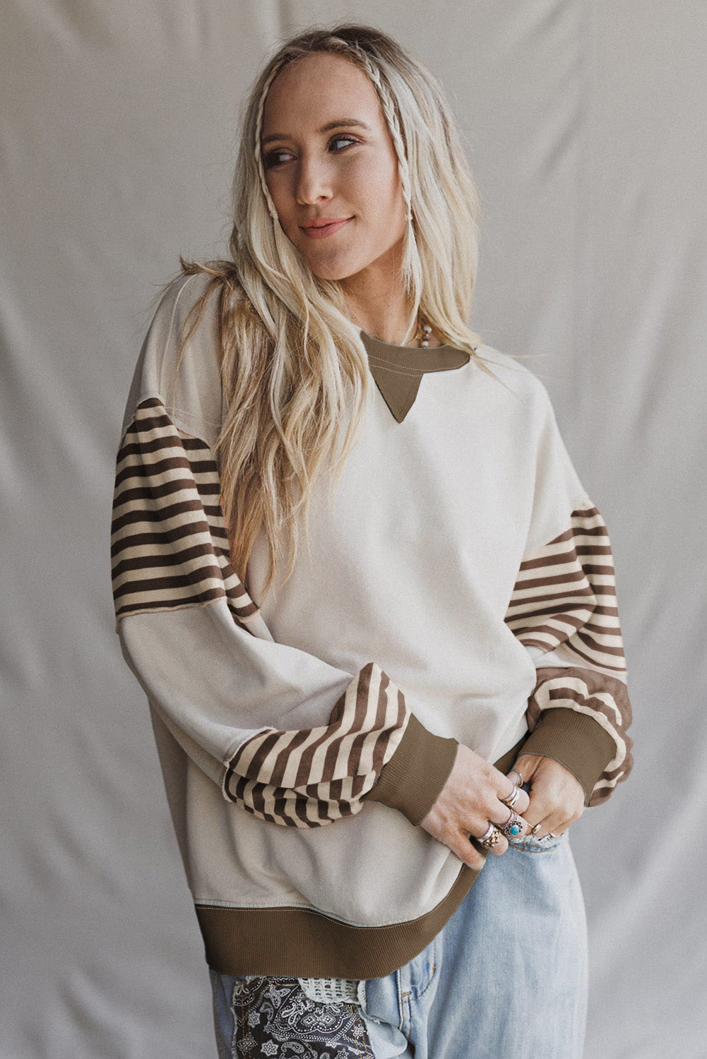 Woman wearing a white sweater with striped sleeves against a plain background