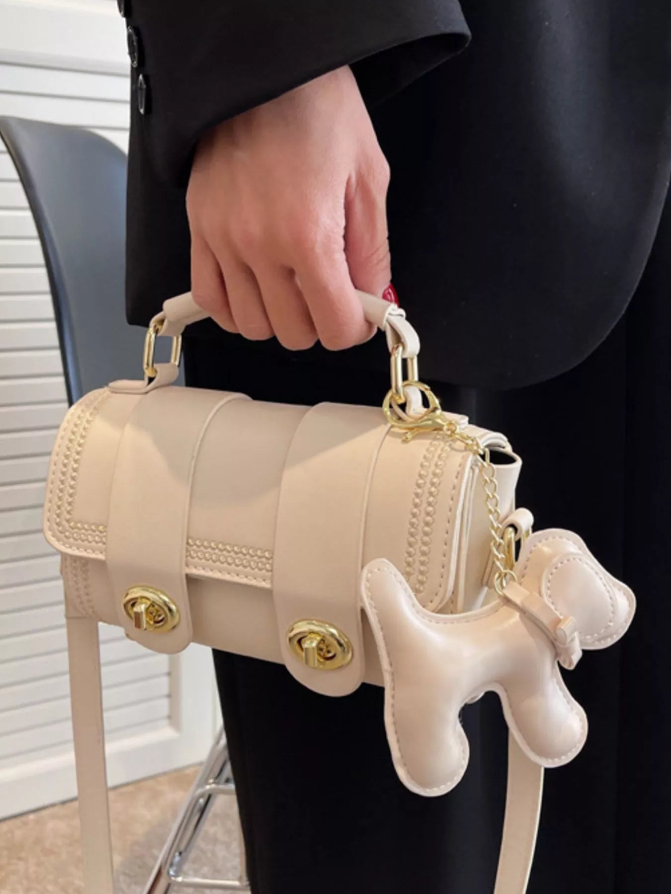 Beige handbag with a dog-shaped charm held by a person.