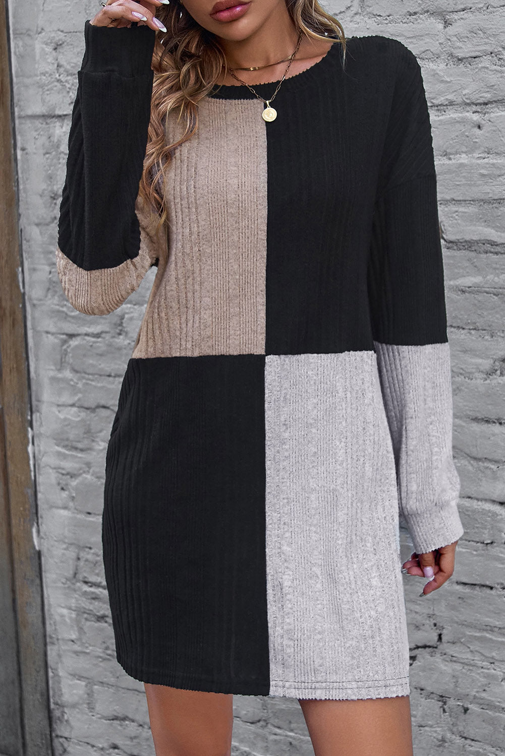 Person wearing a black, beige, and gray checkered dress against a stone wall.