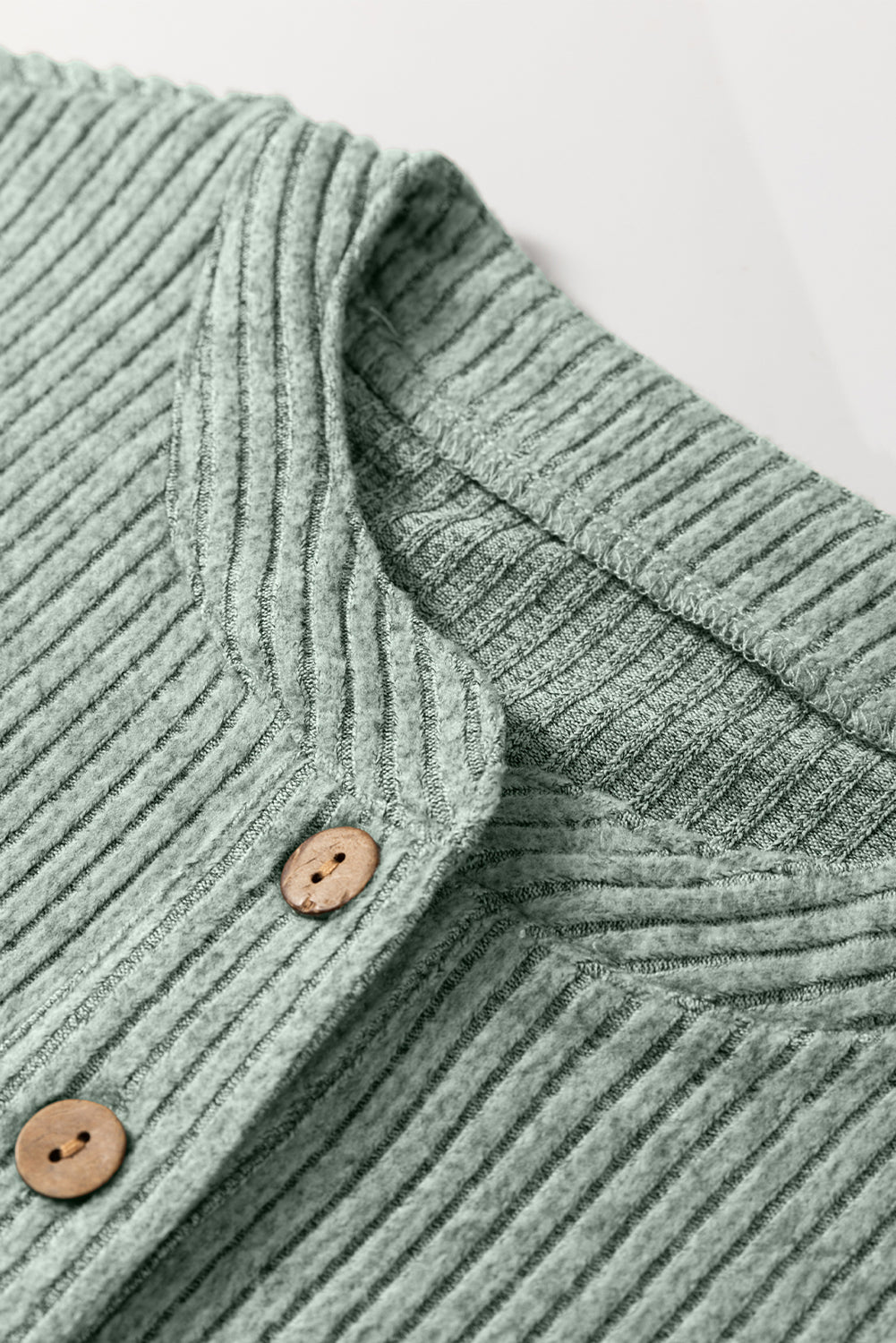 Close-up of a green ribbed sweater with wooden buttons on a light background