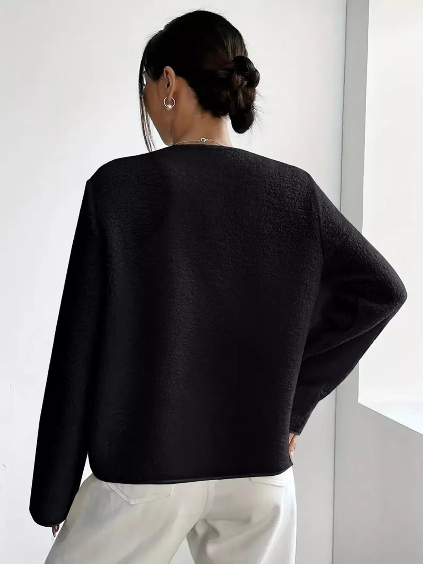 Person wearing a black sweater and white pants against a white background