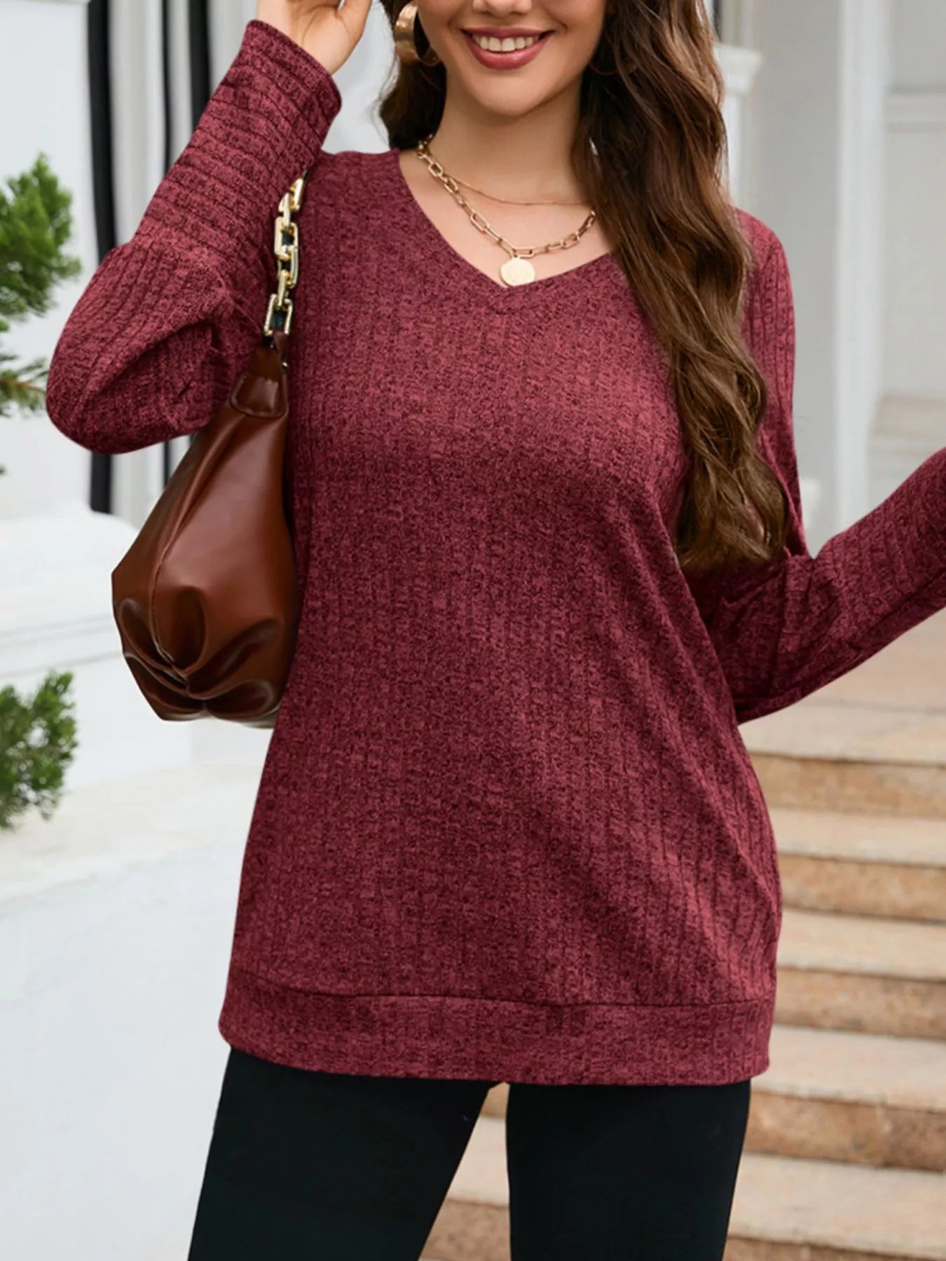 Woman wearing a maroon sweater holding a brown handbag outdoors.