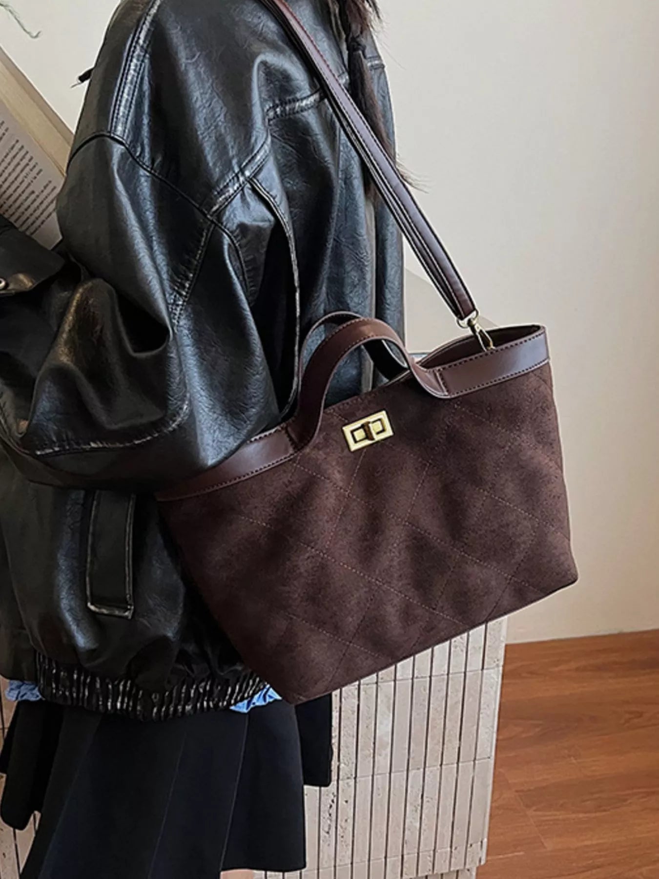 Brown leather handbag held by a person wearing a black leather jacket.
