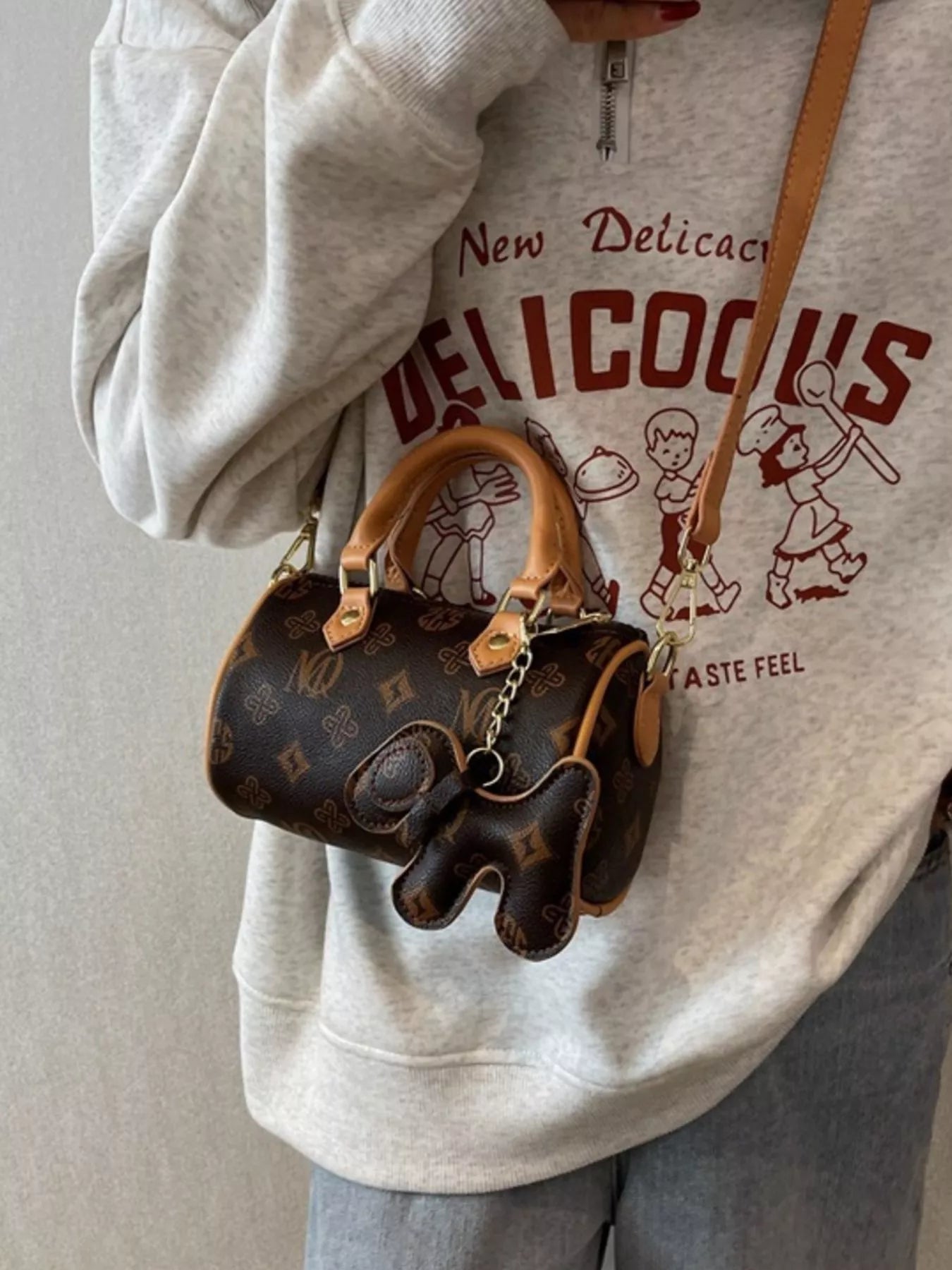 Person wearing a light gray sweatshirt with a graphic design, holding a brown patterned handbag.
