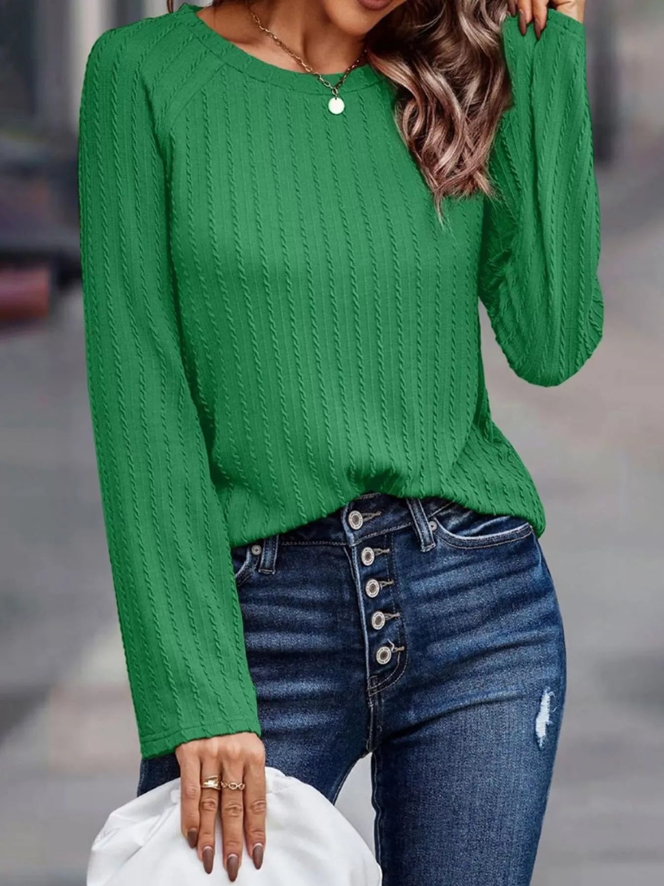 Person wearing a green sweater and blue jeans with a blurred background