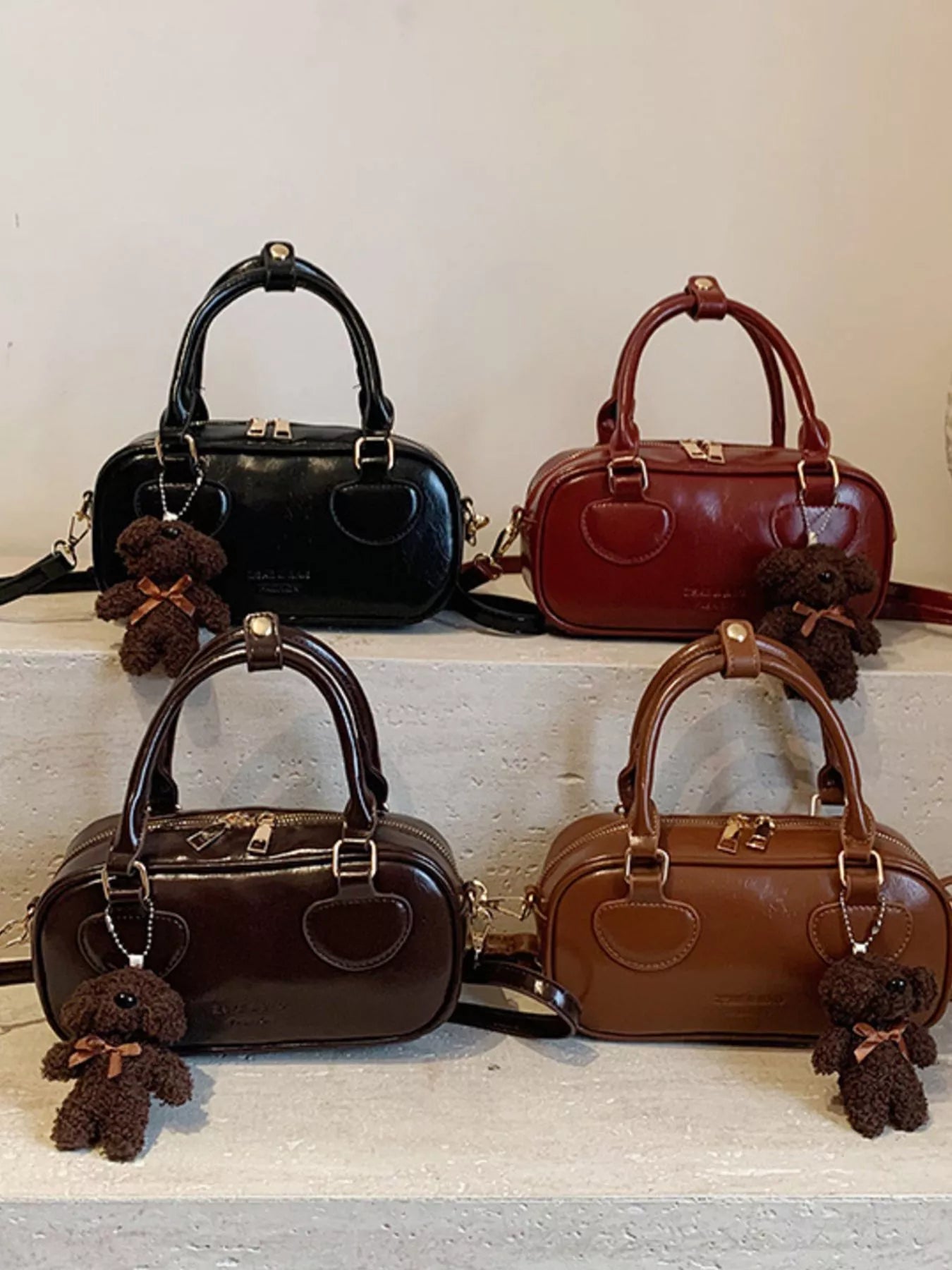 Four handbags in black, brown, and red with teddy bear keychains on a white surface.