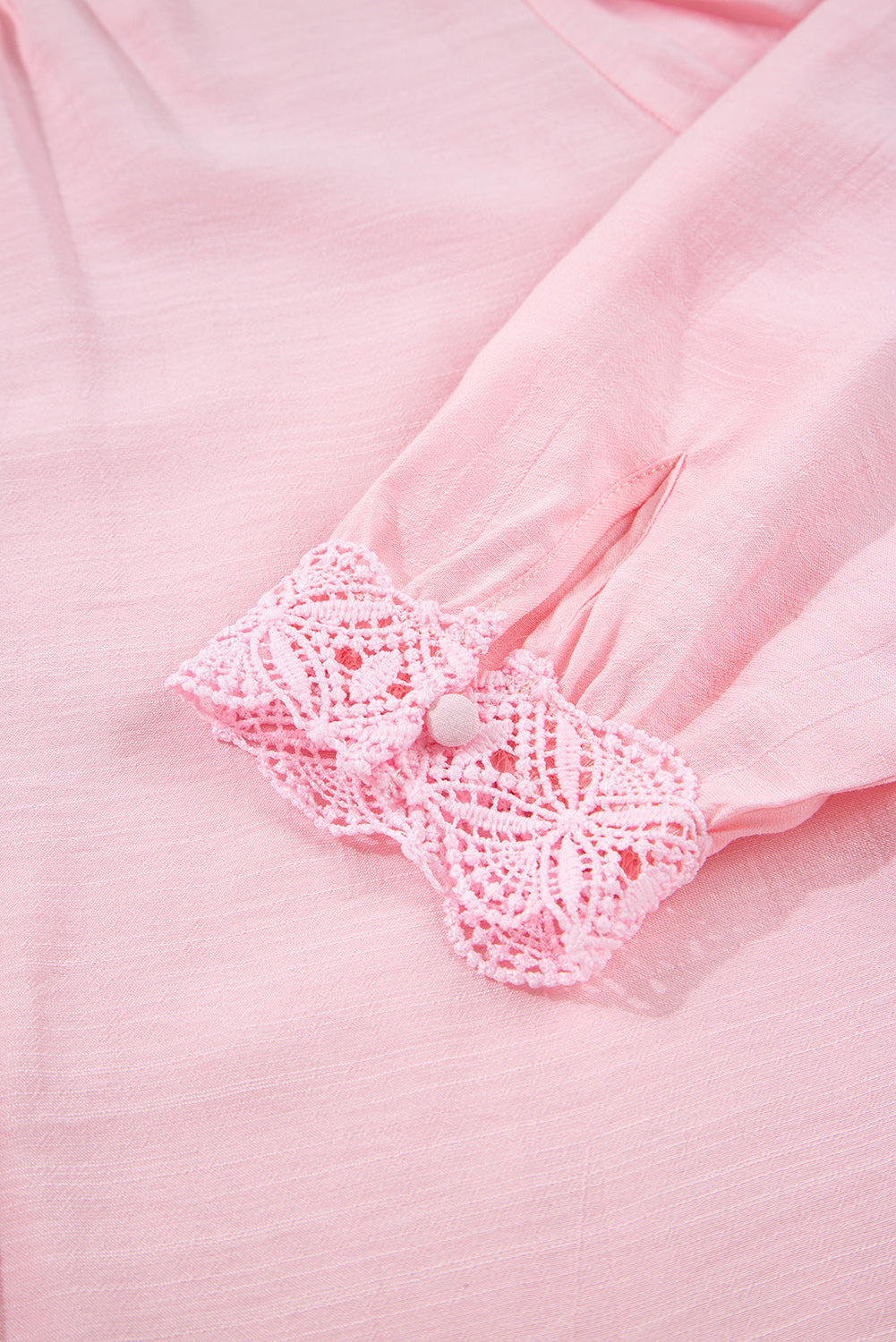 Close-up of a pink garment with a crocheted bow detail on a matching pink background.
