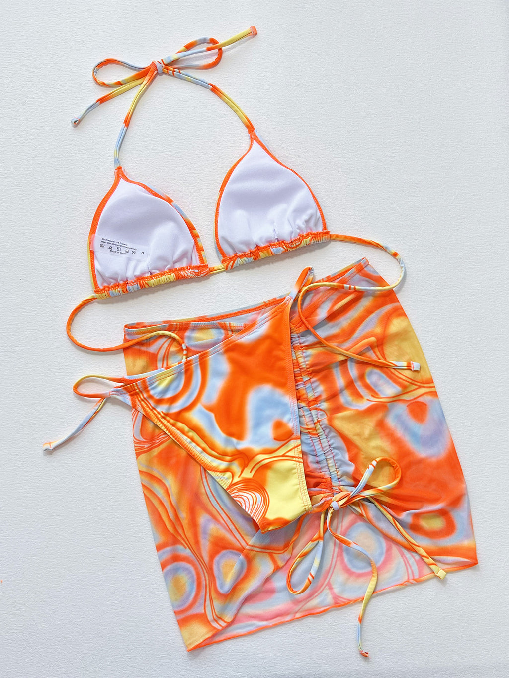 Colorful bikini set with orange, yellow, and white pattern on a light gray background