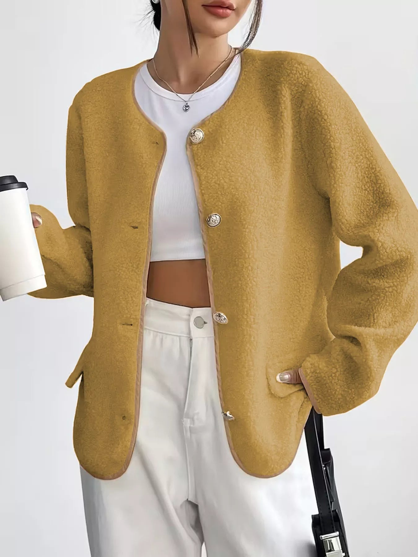 Person wearing a mustard yellow cardigan over a white top and pants, holding a coffee cup.