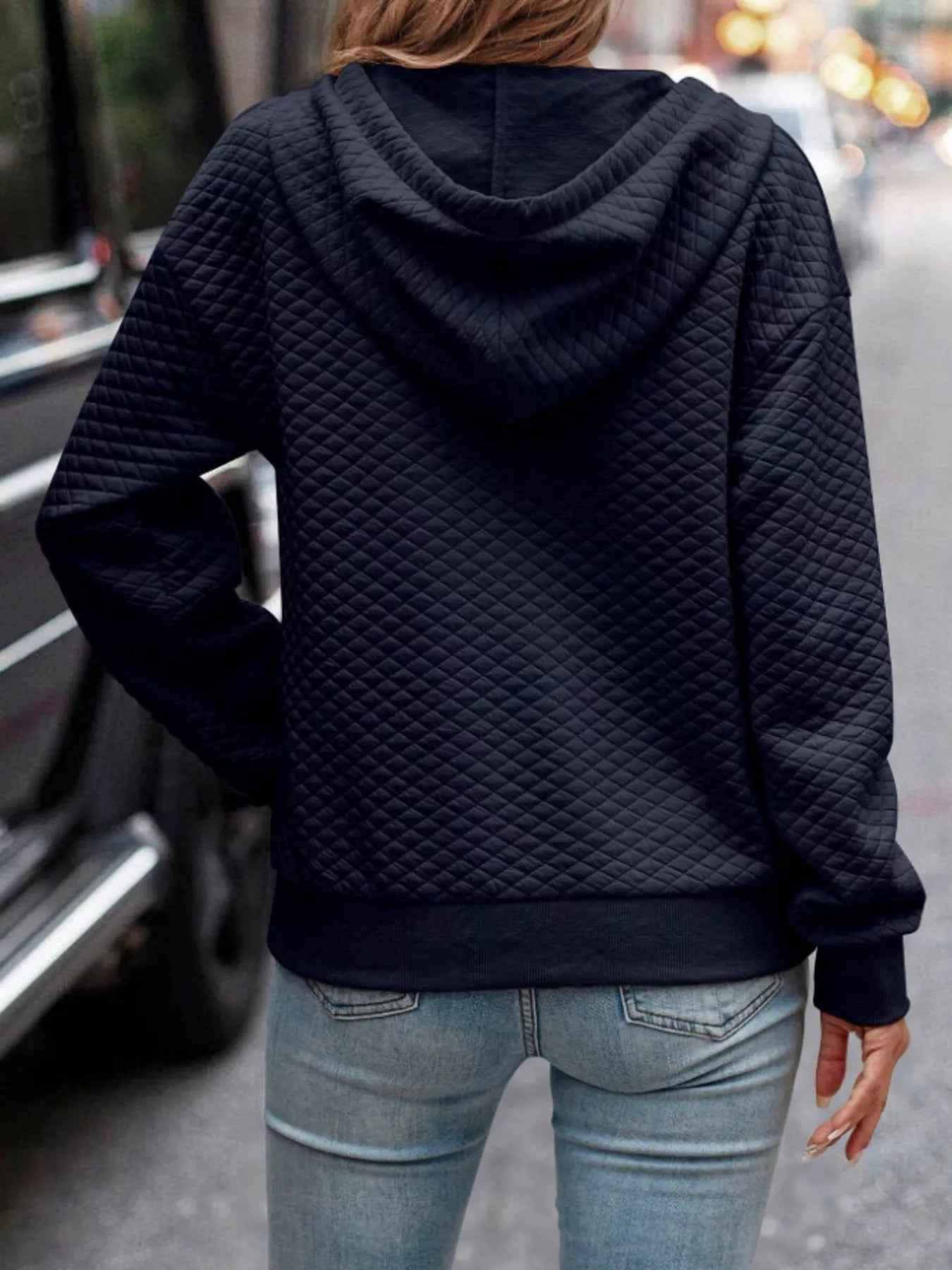 Person wearing a dark quilted hoodie and light blue jeans on a street.