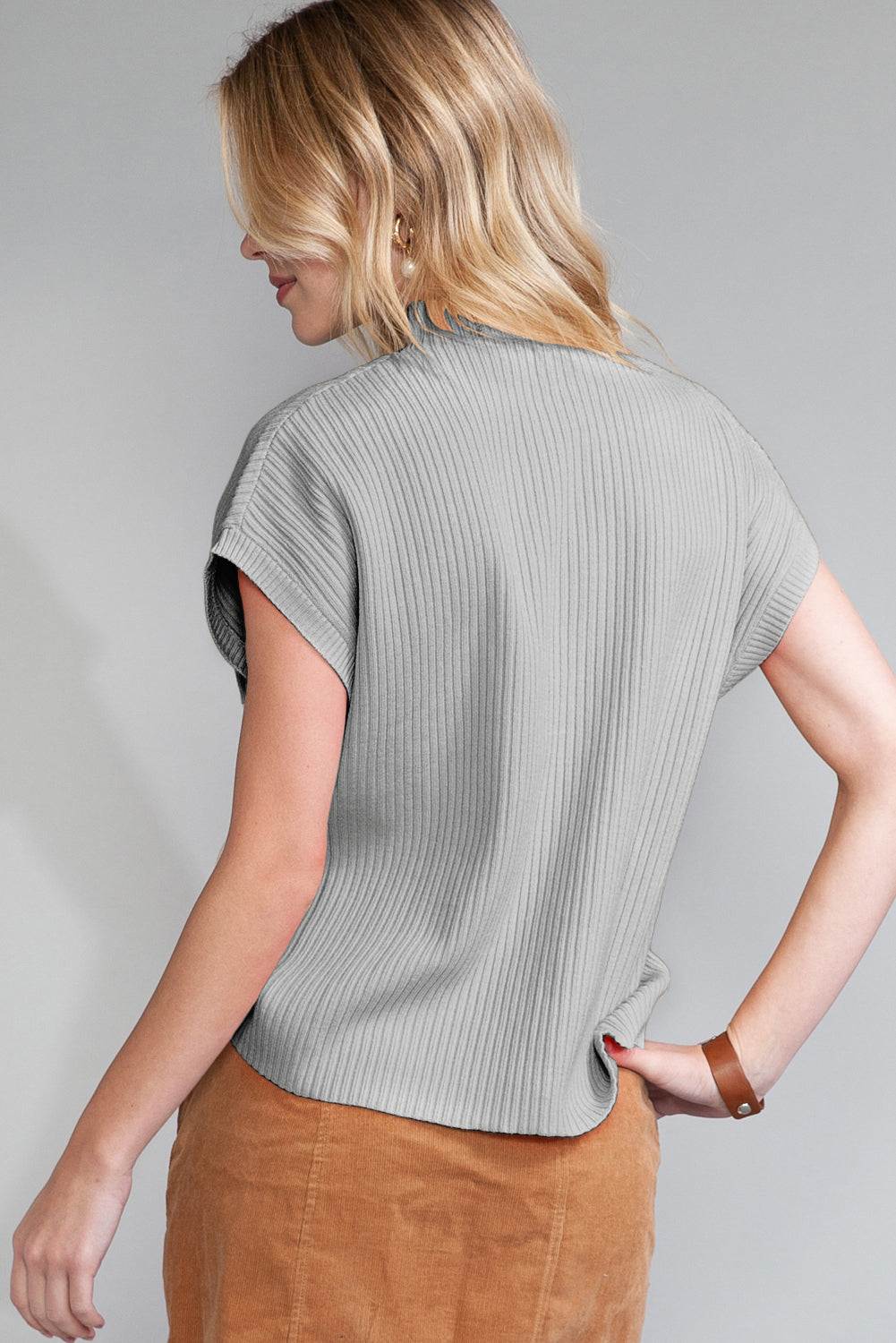 Woman wearing a gray ribbed top and brown pants against a plain background