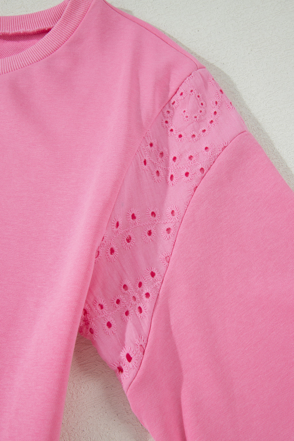 Pink sweatshirt with perforated shoulder design on a light background