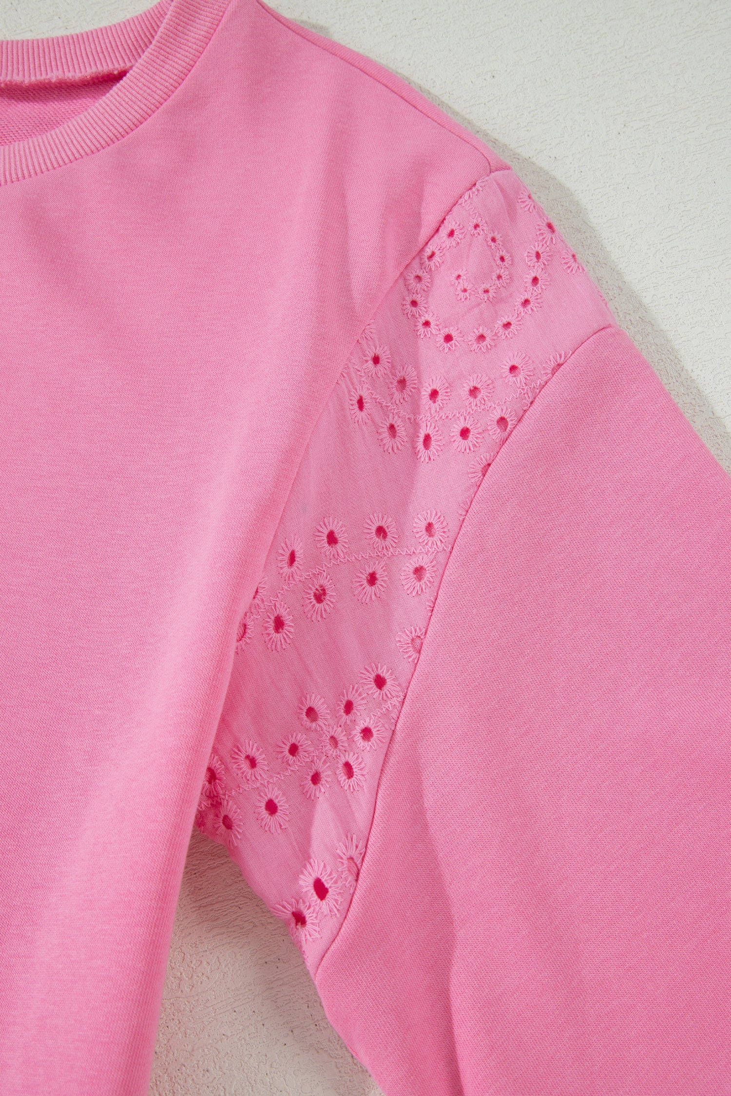 Pink sweatshirt with perforated shoulder design on a light background