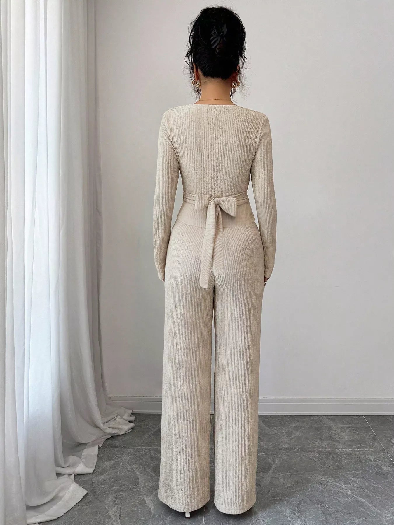 Person wearing a beige ribbed jumpsuit with a belt in a minimalistic setting.