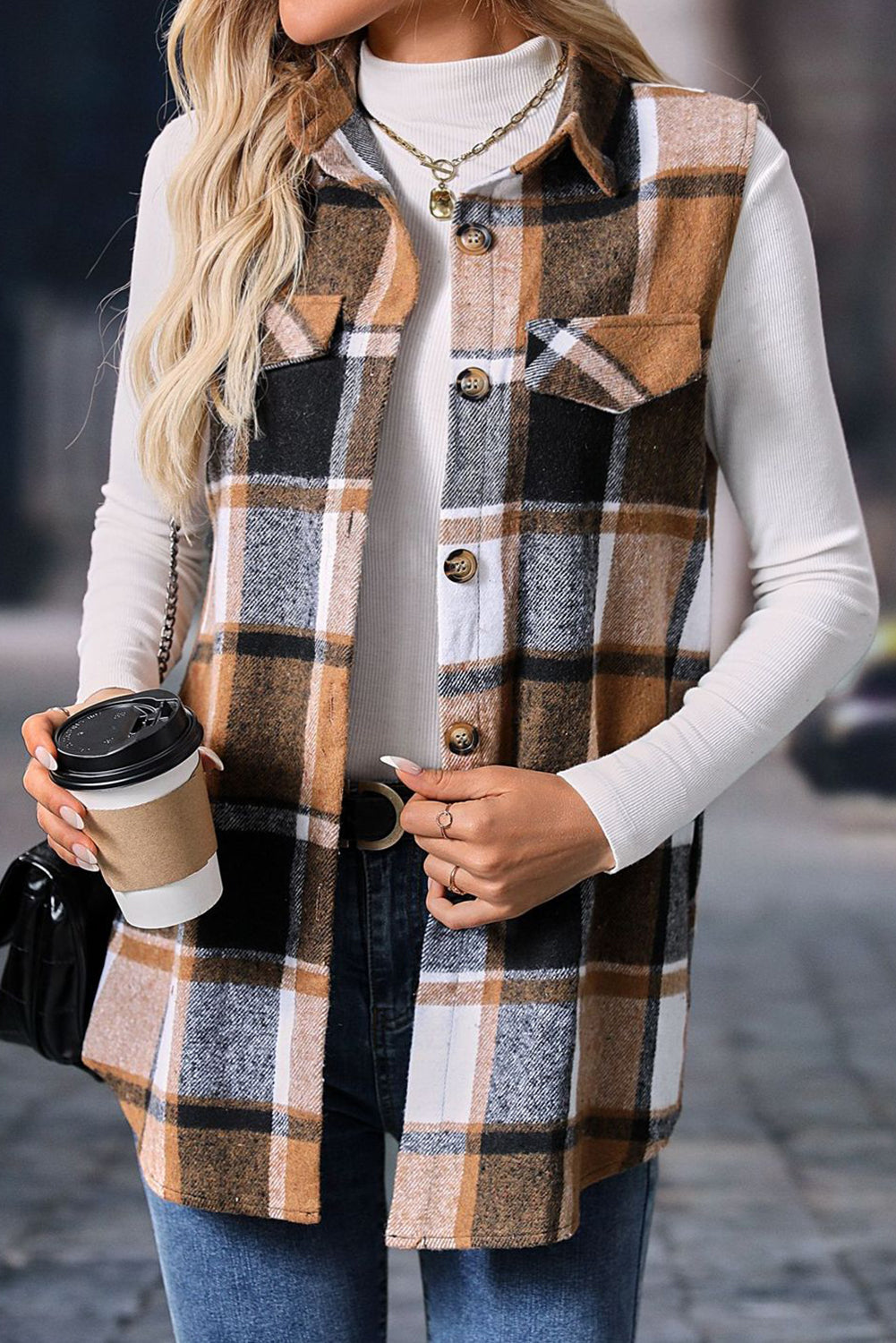 Person wearing a plaid vest over a white long-sleeve shirt, holding a coffee cup.