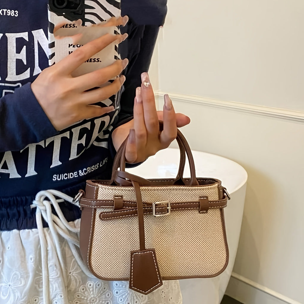 Person holding a beige handbag with brown accents, wearing a dark blue jacket with white text.