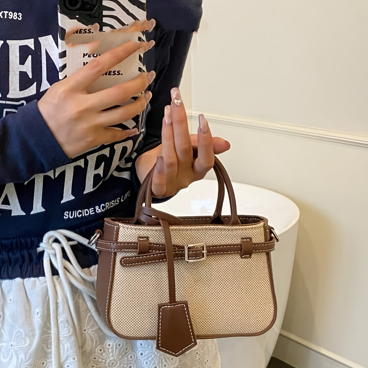 Person holding a beige handbag with brown accents, wearing a dark blue jacket with white text.