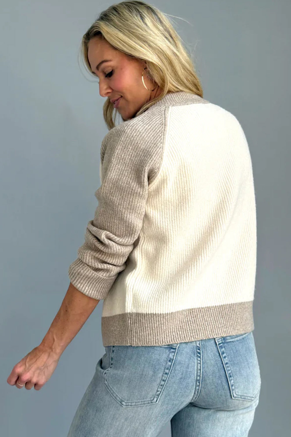 Woman wearing a beige and white sweater with blue jeans against a gray background