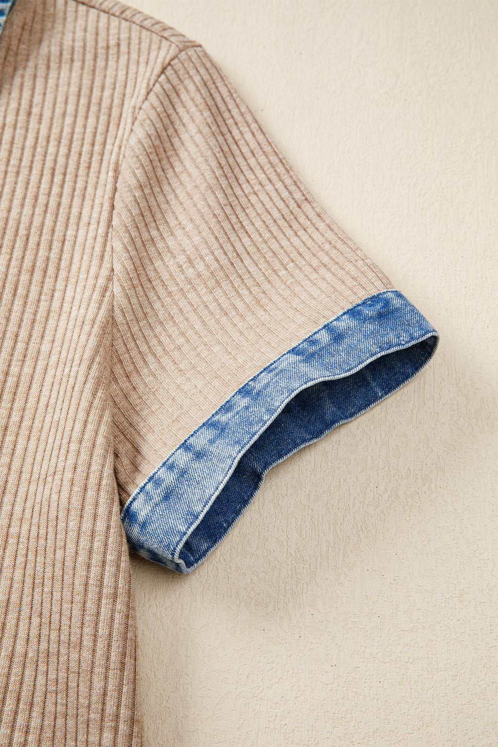 Close-up of a beige sweater with blue denim trim on a beige background