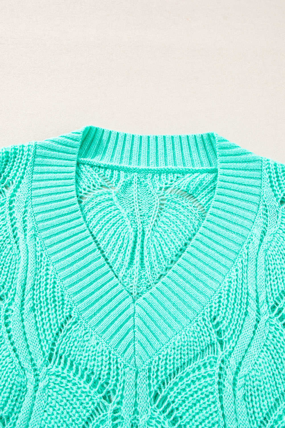 Close-up of a teal knitted sweater on a beige background