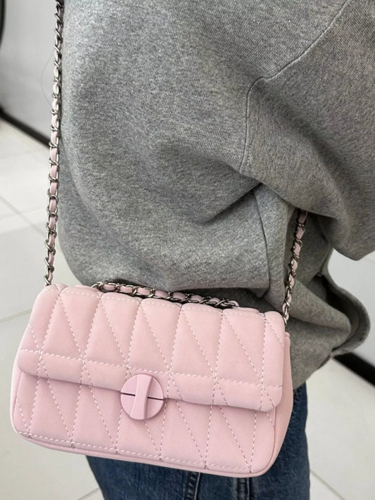 Pink quilted handbag with a chain strap held by a person wearing a gray sweatshirt.