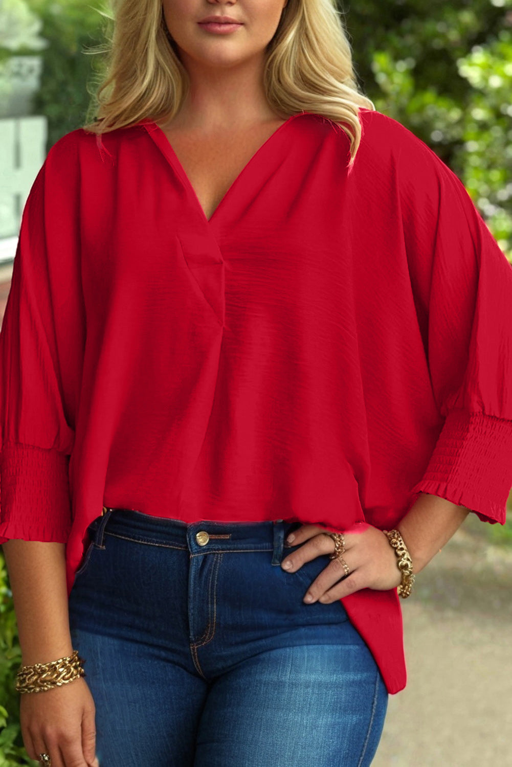 Person wearing a red blouse and blue jeans with a blurred green background