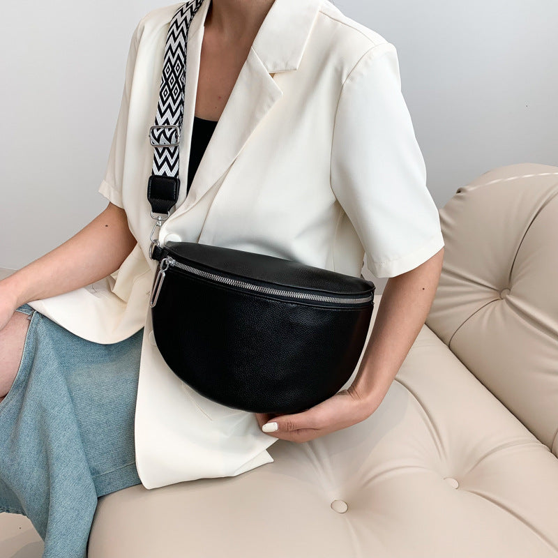 Person holding a black waist bag with a patterned strap on a neutral background