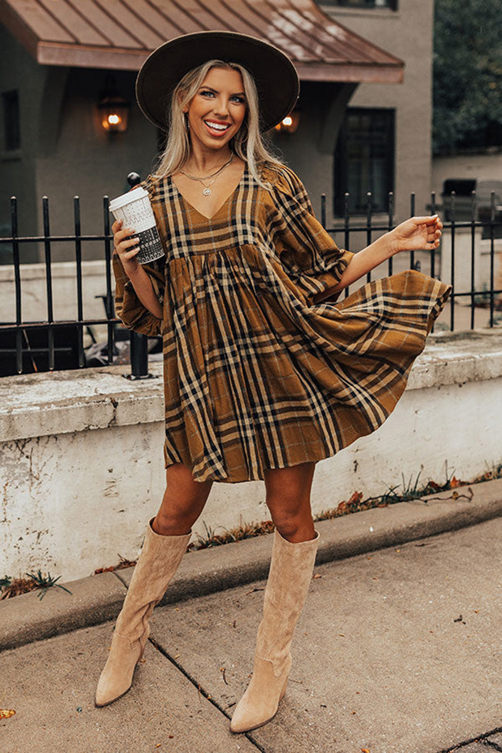 Woman in plaid dress and beige boots standing on a sidewalk.