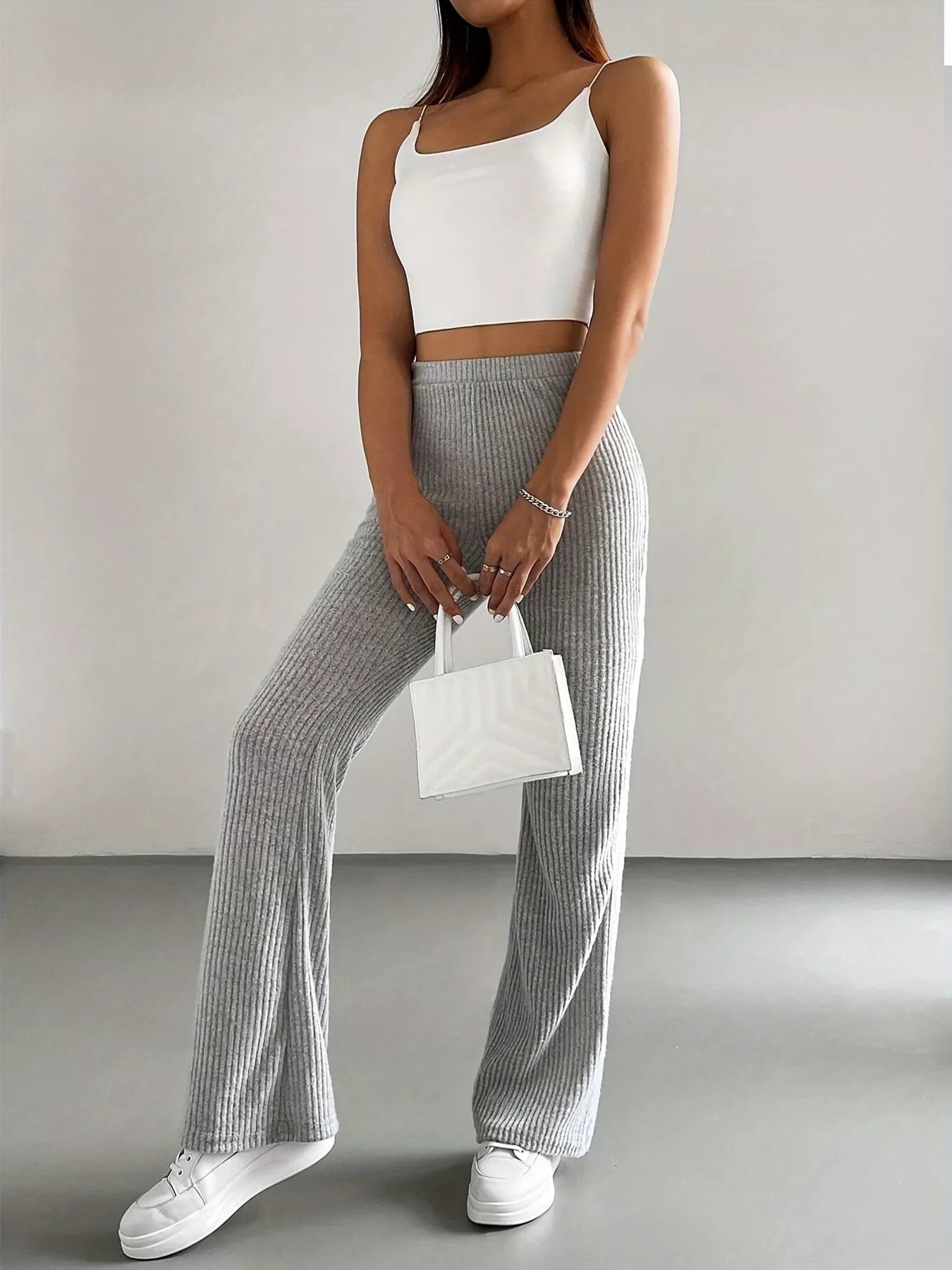 Person wearing a white top and gray checkered pants holding a small white handbag against a plain background