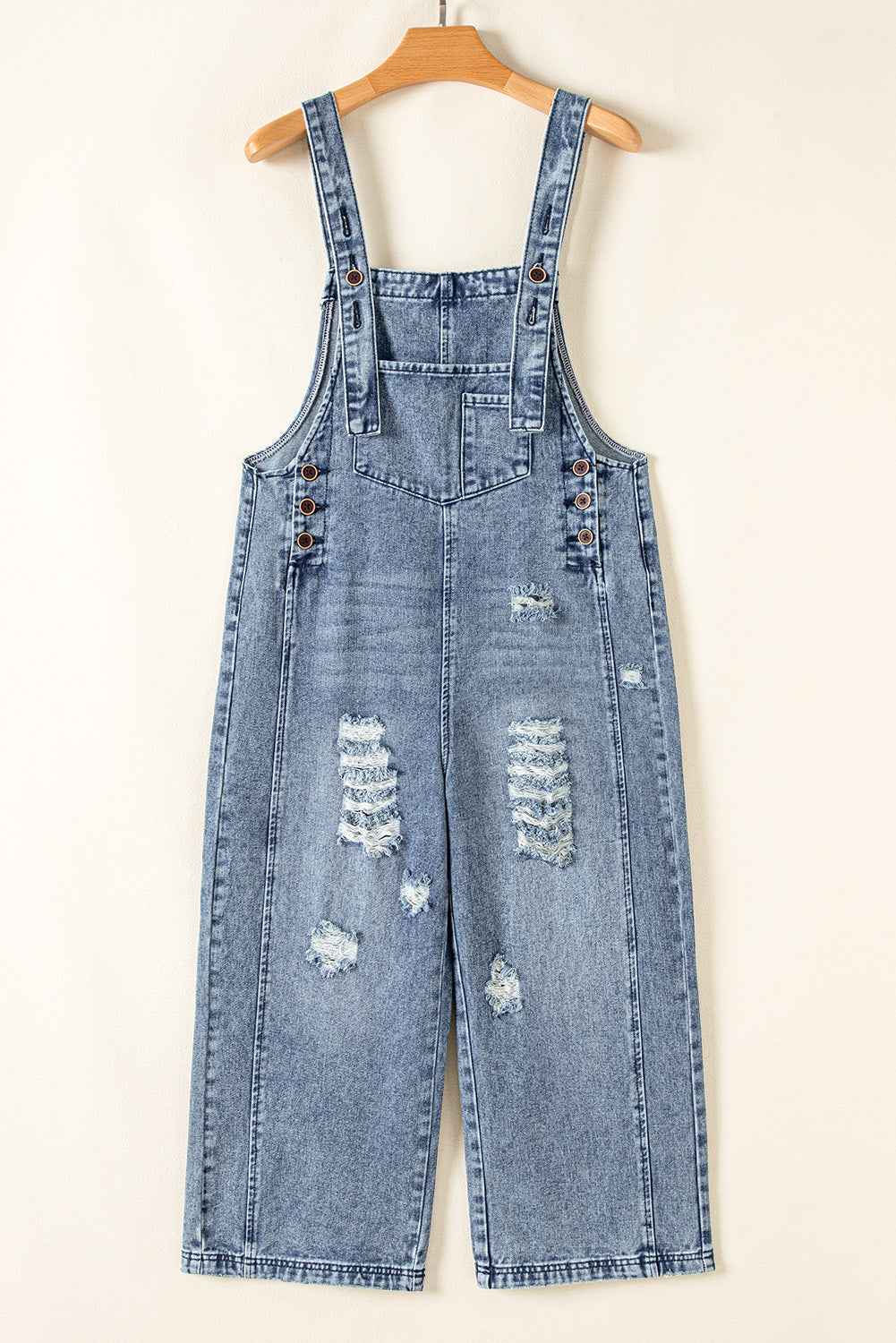 Denim overalls with distressed details on a hanger against a white background