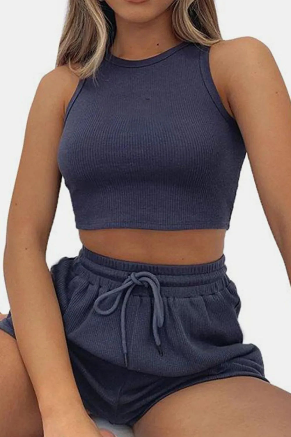 Person wearing a navy blue crop top and shorts set on a light gray background