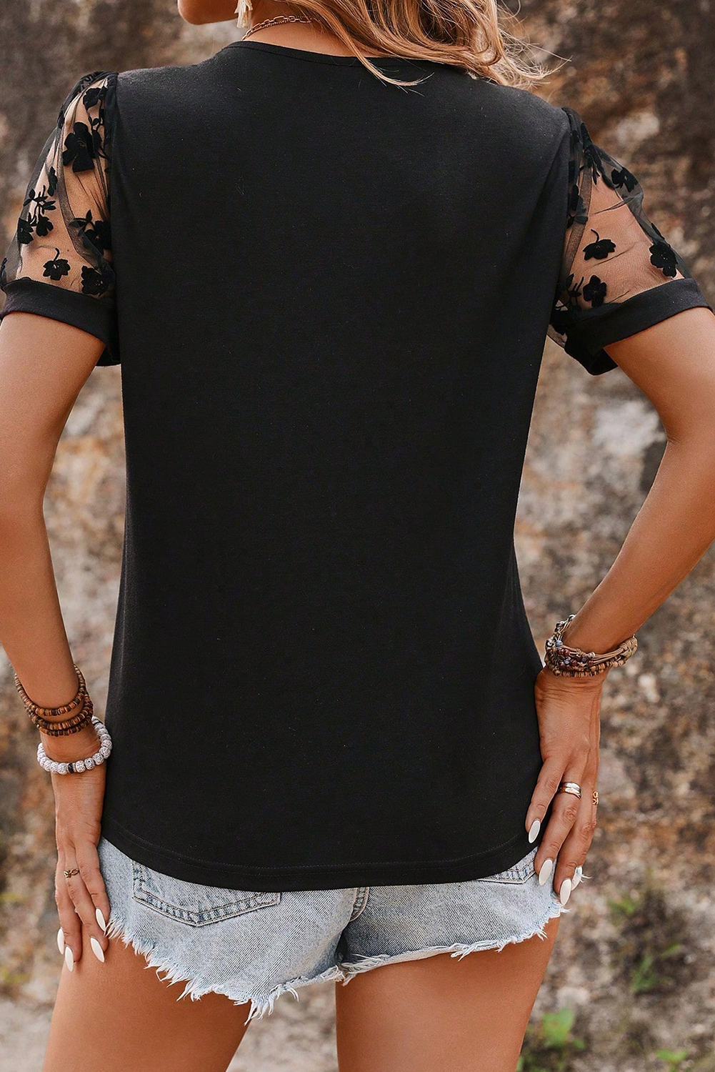 Black sleeveless top with floral lace details on sleeves worn by a person.