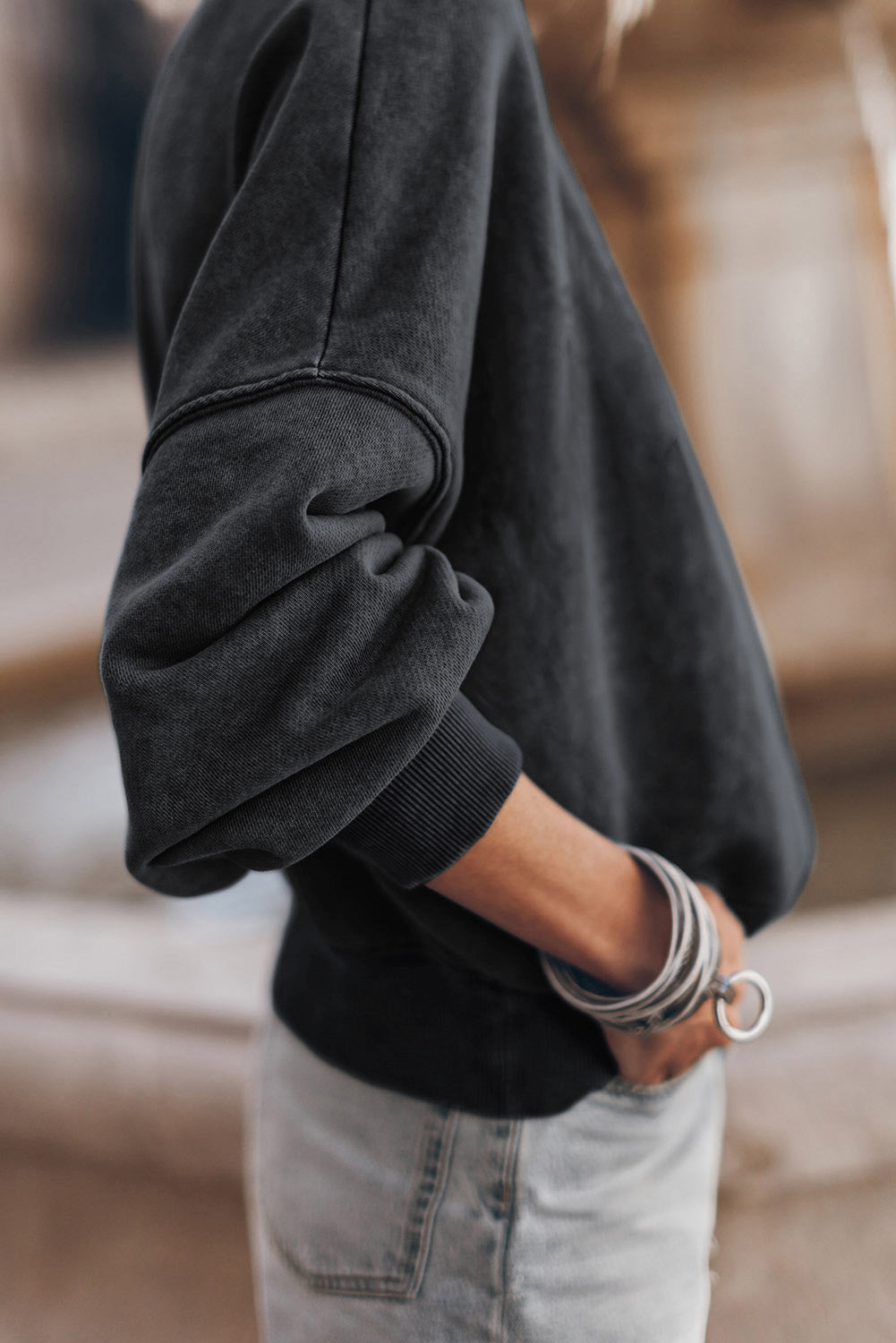 Person wearing a black sweater and light jeans with bracelets on a blurred background