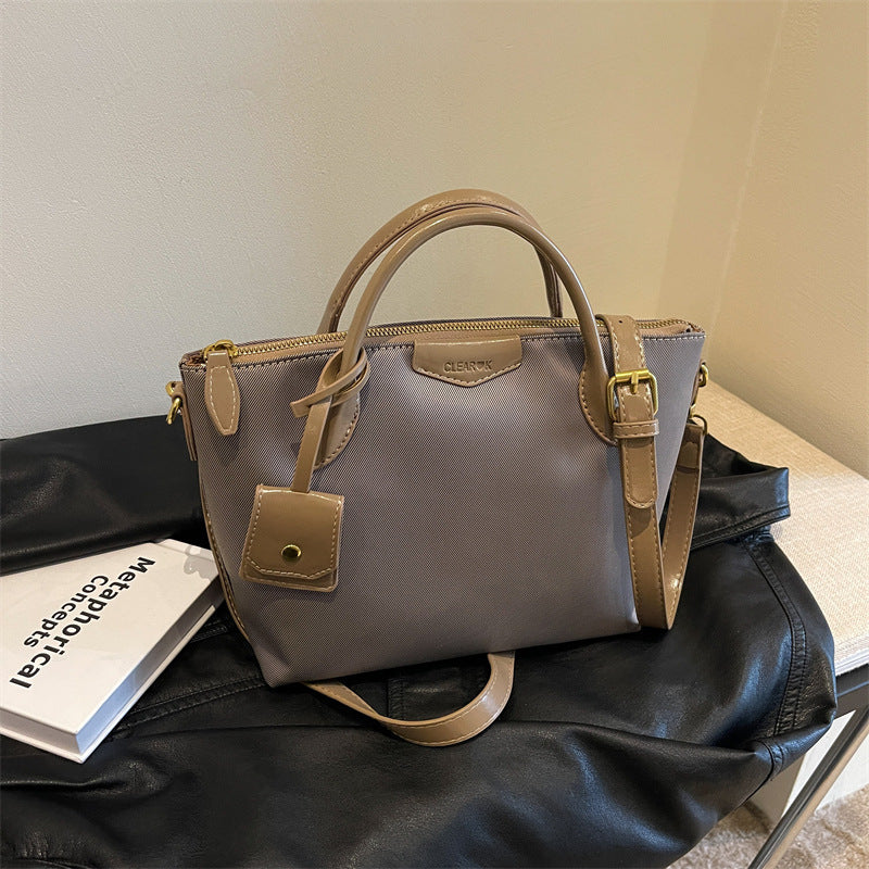 Gray handbag with brown handles and accents on a black surface.