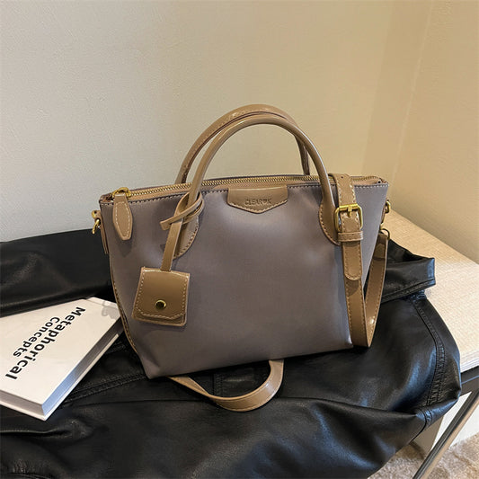 Gray handbag with brown handles and accents on a black surface.