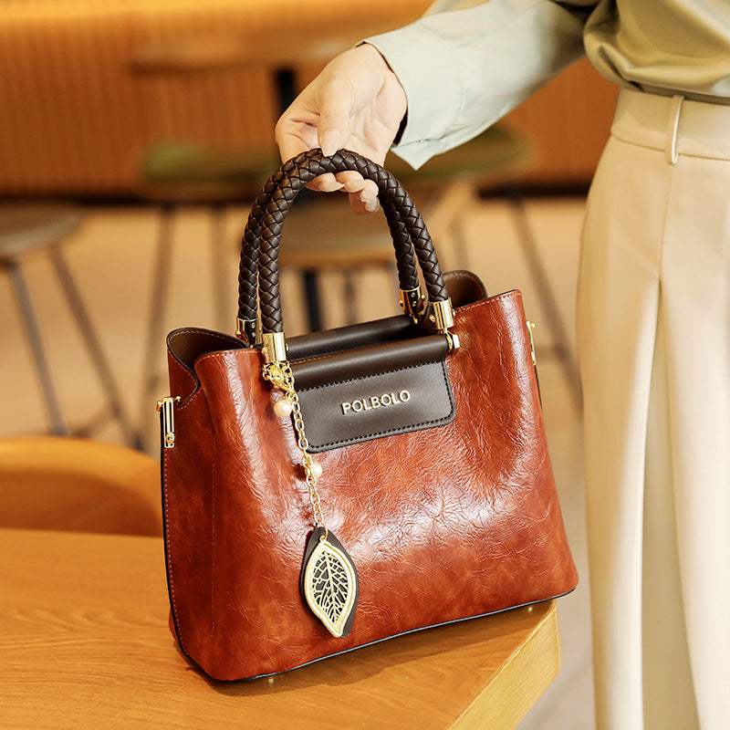 Brown handbag with braided handle held by a person in an indoor setting