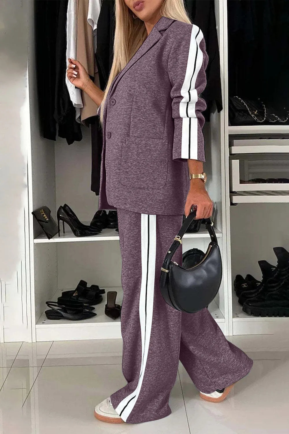 Woman in a purple tracksuit with white stripes holding a black handbag in a room with shelves of shoes.